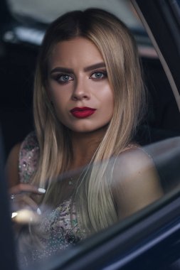 Şatafatlı, zengin, seksi, makyajlı bir kadın arabada oturup pencereden bakıyor. Parti için hazır. Akşam portresi.