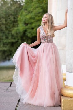 Parkta makyajlı sarışın bir kadın. Elbisesinin eteği rüzgarda uçuşuyor. Gün batımı ışığında şehvetli moda portresi.