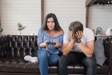 Erkek, kadınına joystick ile nasıl oyun oynanacağını öğretiyor. Kadınlar neşeyle gülümser. Rahat bir evde dinleniyorlar..