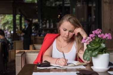 Kafede oturup kahve içen ve gündemini planlayan bir kadın. Güzel bir yerde tek başına, rahatlıyor ve geleceği hayal ediyor.
