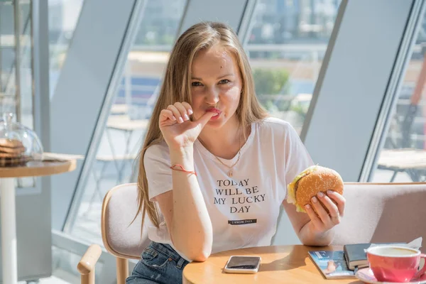 可愛いです陽気な女性食べる不健康なハンバーガーでA Caf Amd笑顔喜んで — ストック写真