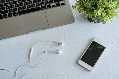 dizüstü bilgisayar, cep telefonu ve kulaklıklar beyaz arka planda bir masanın üzerinde duruyor.