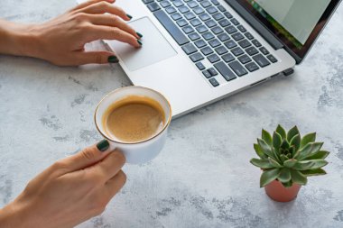 Bir kız elinde bir kupa kahve tutuyor, masanın yanında bir laptop var.