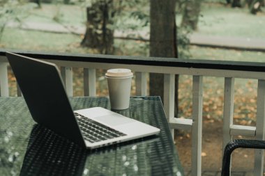 Parktaki bir kafede üzerinde kahve olan bir laptop ve bir kupa var.