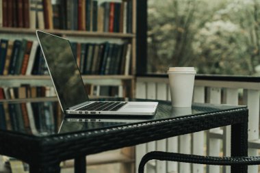 Parktaki bir kafede üzerinde kahve olan bir laptop ve bir kupa var.