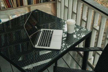 Parktaki bir kafede üzerinde kahve olan bir laptop ve bir kupa var.