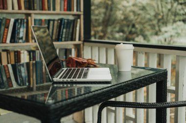 Parktaki bir kafede üzerinde kahve olan bir laptop ve bir kupa var.