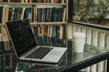 Parktaki bir kafede üzerinde kahve olan bir laptop ve bir kupa var.