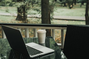Parktaki bir kafede üzerinde kahve olan bir laptop ve bir kupa var.