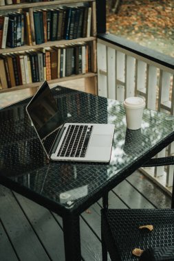 Parktaki bir kafede üzerinde kahve olan bir laptop ve bir kupa var.