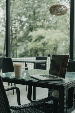 Parktaki bir kafede üzerinde kahve olan bir laptop ve bir kupa var.