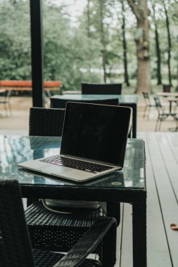 Parktaki bir kafede üzerinde kahve olan bir laptop ve bir kupa var.