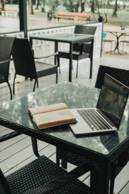 Bir kafede, açık bir kitabın yanında, masanın üstünde bir laptop var.