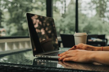 Kız bir kafede oturuyor ve dizüstü bilgisayarda klavye yazıyor. Yakınlarda bir fincan kahve var.