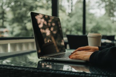 Kız bir kafede oturuyor ve dizüstü bilgisayarda klavye yazıyor. Yakınlarda bir fincan kahve var.