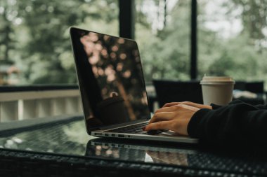 Kız bir kafede dizüstü bilgisayarın yanında oturuyor. Yakınlarda bir bardak kahve var.