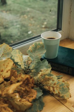 Masanın üzerinde bir bardak kahve var, yanında da akçaağaç yaprakları.