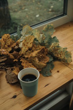 Masanın üzerinde bir bardak kahve var, yanında da akçaağaç yaprakları.