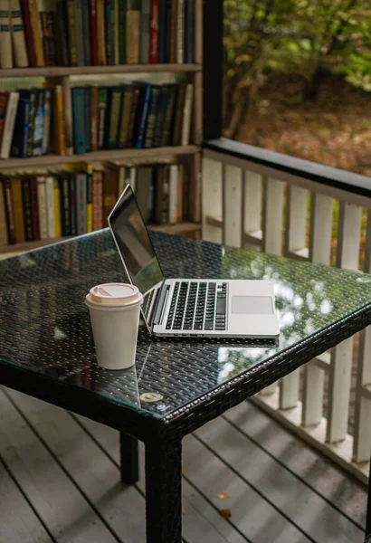 Parktaki bir kafede üzerinde kahve olan bir laptop ve bir kupa var.