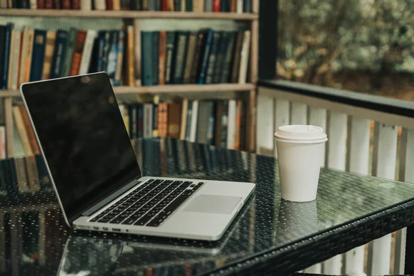 Parktaki bir kafede üzerinde kahve olan bir laptop ve bir kupa var.