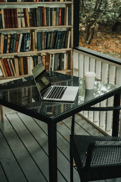 Parktaki bir kafede üzerinde kahve olan bir laptop ve bir kupa var.