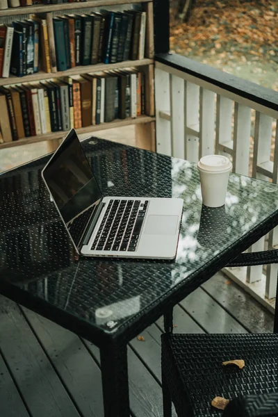 Parktaki bir kafede üzerinde kahve olan bir laptop ve bir kupa var.