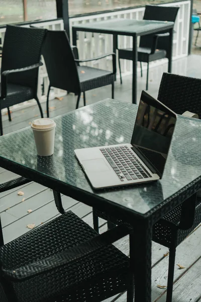 there is a laptop and a mug with coffee on the table in a cafe in the park