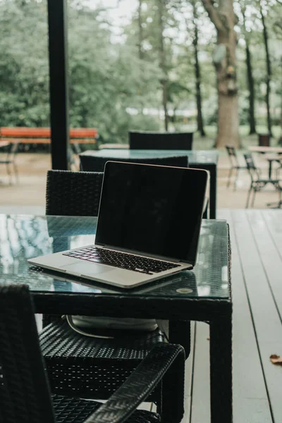 Parktaki bir kafede üzerinde kahve olan bir laptop ve bir kupa var.