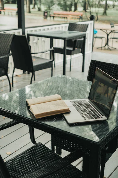 Bir kafede, açık bir kitabın yanında, masanın üstünde bir laptop var.