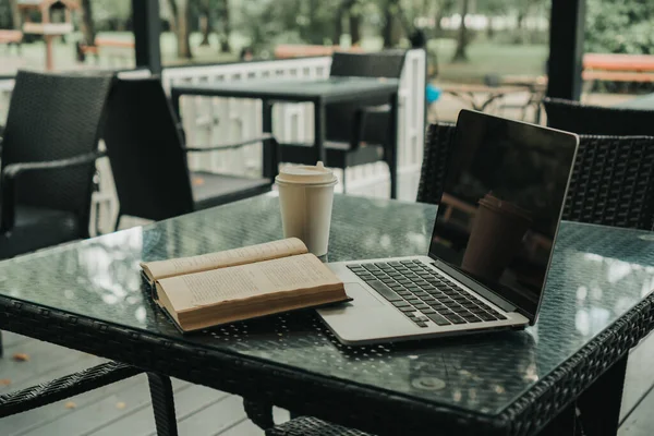 Bir kafede, açık bir kitabın yanında, masanın üstünde bir laptop var.