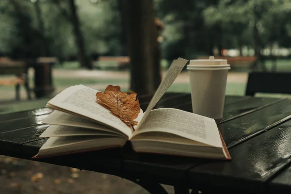 Açık bir kitap sonbahar akçaağaç yaprağı olan bir masanın üzerinde yatıyor.