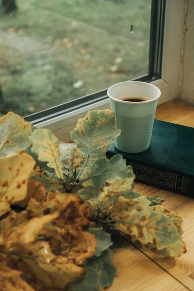 Masanın üzerinde bir bardak kahve var, yanında da akçaağaç yaprakları.