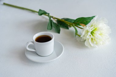 Masanın üzerinde bir kupa kahve var. Çiçeğin yanında.