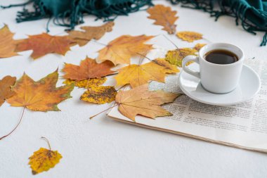 Masanın üzerinde sonbahar yaprakları var, yanında bir kupa kahve ve bir gazete var.