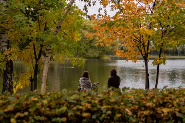 Bir adam ve bir kız, sonbaharda bir parkta göletin kenarında duruyorlar.
