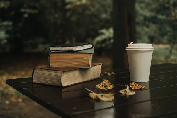 books coffee mug and autumn leaves on the table in the park