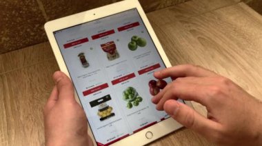 Adamın biri bir online mağazadan tablet kullanarak elma sipariş ediyor. Online mağazadaki ürünlerin seçimi..