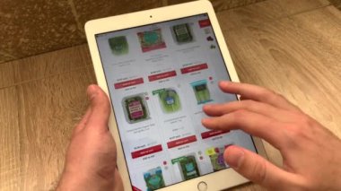 Bir adam online bir dükkanda marul ve diğer yapraklı yeşillikleri tablet kullanarak seçer. Online mağazadaki ürünlerin seçimi..