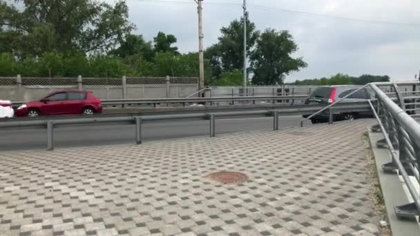 Pociąg metra przejeżdżający obok drogi miejskiej. Ruch samochodowy na ulicy. Transport publiczny. 4K. Kijów, Ukraina. — Wideo stockowe