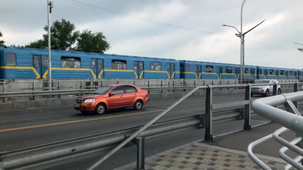 4K. Métro passant sur le pont près de la route de la ville. Les voitures roulent le long du métro le long de l'autoroute. Transports publics. Journée nuageuse d'été. Kiev, Ukraine. — Video