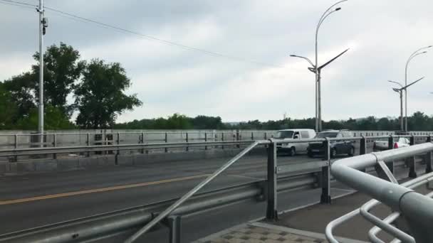 4K. Kiev, Ukraine. Métro et voitures passant sur le pont sur la rivière Dniepr. Les voitures roulent le long du métro le long de l'autoroute. Transports publics. Journée nuageuse d'été. Mouvement horizontal de la caméra. — Video