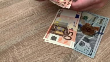 Bitcoin şifreleme parasının satın alınması için el ile büyük miktarda nakit para sayan bir adamın yakın çekimi. 100 Amerikan doları ve 50, 10, 5 avroluk banknotları sayıyorum. 4K.