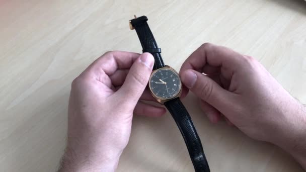 Nahaufnahme. Ein Mann stellt auf einer Armbanduhr aus Vintage-Gold mit schwarzem Lederarmband die richtige Zeit ein. Zeiger mechanischer Uhren aufziehen. — Stockvideo