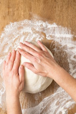 Kadın eli, pizza hamurunu ahşap bir masada yoğurur.