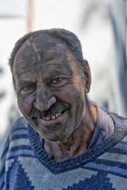 Yüzü siyah toz içinde gülümseyen yaşlı bir adam.