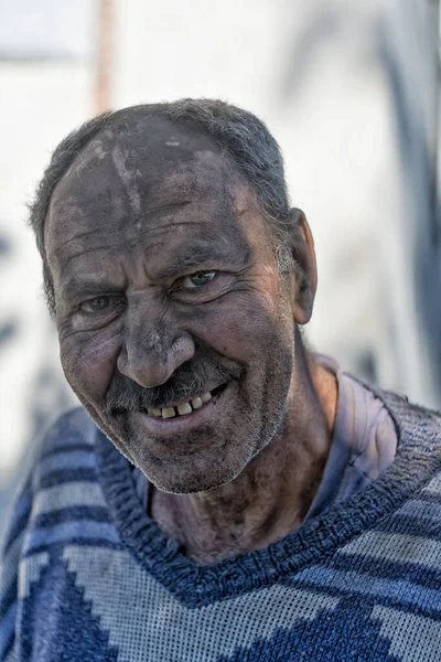 Yüzü siyah toz içinde gülümseyen yaşlı bir adam.