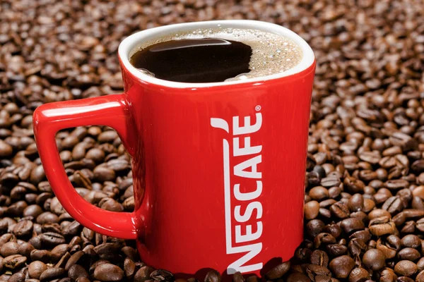 Röd mugg av Nescafe på bakgrunden av spridda kaffebönor — Stockfoto