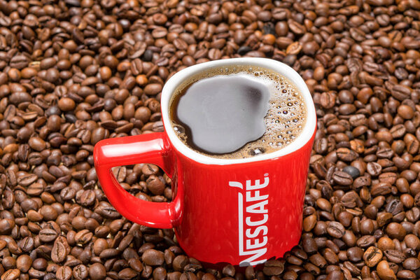 red mug of Nescafe on the background of scattered coffee beans