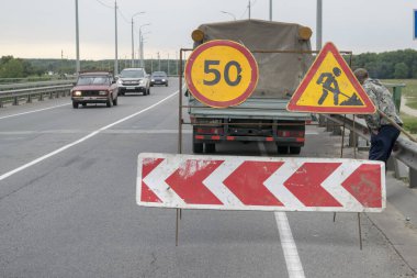 Nehrin üzerindeki köprüde yol çalışmaları devam ediyor. İşçilerin güvenliği için uyarı işaretleri gösterilir.