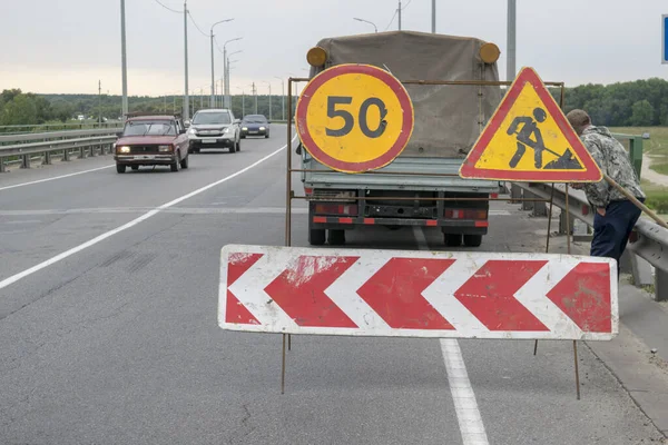 Road works are underway on the bridge over the river. For the safety of workers, warning signs are displayed.